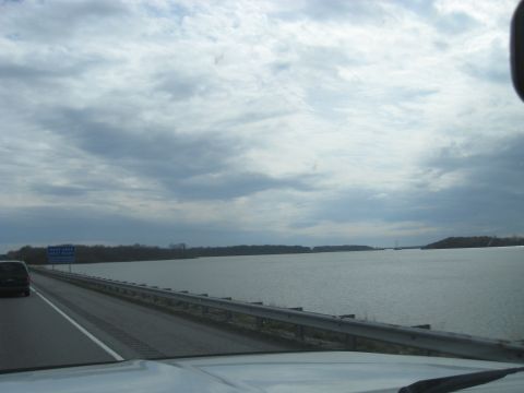 1978 Ford Bronco - View from a vehicle traveling on a highway alongside a wide expanse of water under an overcast sky.