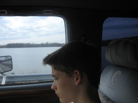 1978 Ford Bronco - View from inside a vehicle shows a person looking out the window at a calm body of water and trees on the horizon.