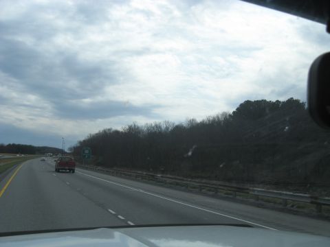 1978 Ford Bronco - A red pickup truck travels down a highway on an overcast day.