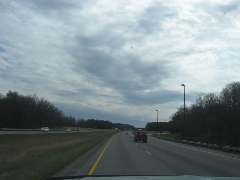 1978 Ford Bronco - A view from a vehicle traveling on a highway under a cloudy sky, with trees lining the sides of the road and other cars visible.