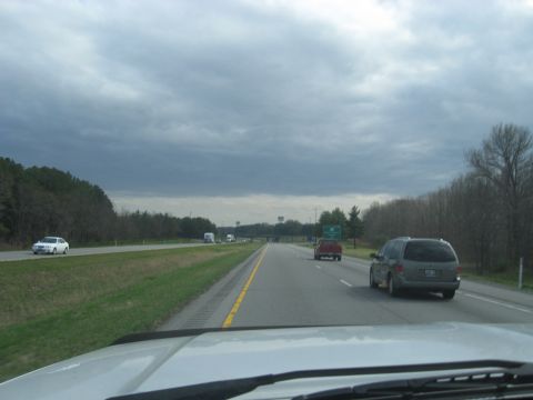 1978 Ford Bronco - A gray minivan travels down a highway with other vehicles and trees lining the road.