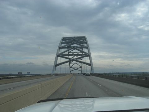 1978 Ford Bronco - Driving across a large steel arch bridge on a highway with a cloudy sky overhead.