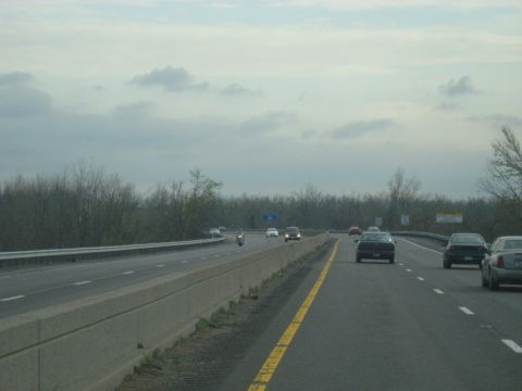 1978 Ford Bronco - Multiple vehicles travel on a highway with trees lining the median and roadside.