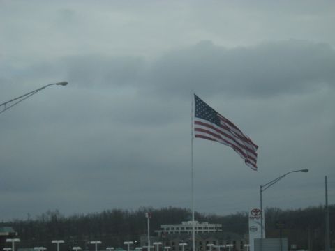 1978 Ford Bronco - An American flag flies high under a cloudy sky, with a Toyota dealership sign in the background.