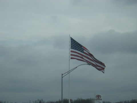 1978 Ford Bronco - An American flag flies proudly under a cloudy sky, with a Toyota dealership sign in the distance.