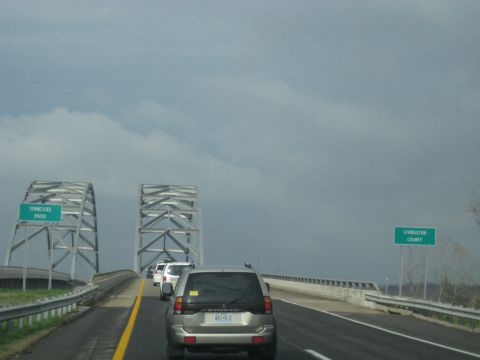 1978 Ford Bronco - A silver SUV drives across a bridge under a cloudy sky, with signs indicating the Tennessee River and Livingston County.