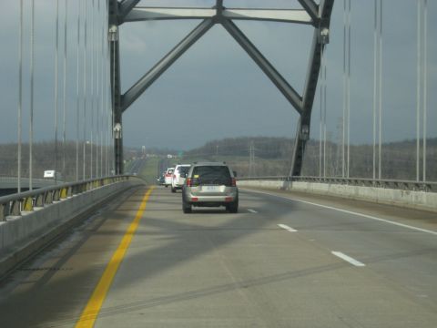 1978 Ford Bronco - A silver SUV travels across a bridge, joining a line of other vehicles under a dramatic, overcast sky.