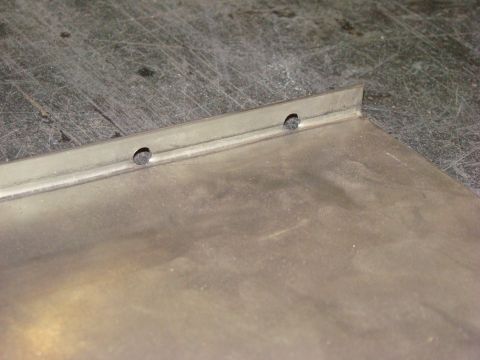 1948 Jeep Wrangler - Close-up of a metal panel with two holes, possibly for rivets or fasteners, on a workbench.