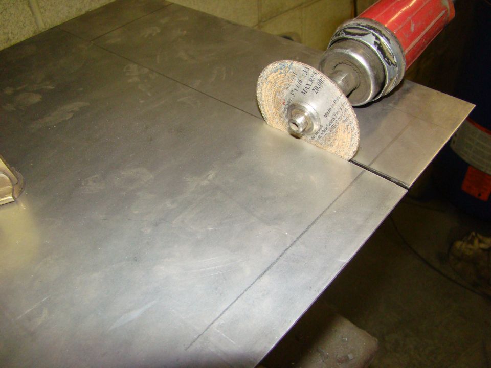 Grinding disc on a metal sheet with cut lines, red tool handle visible