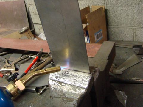 1948 Jeep Wrangler - A metal sheet is held in a vise and heated with a torch, with various tools and a cardboard box visible.