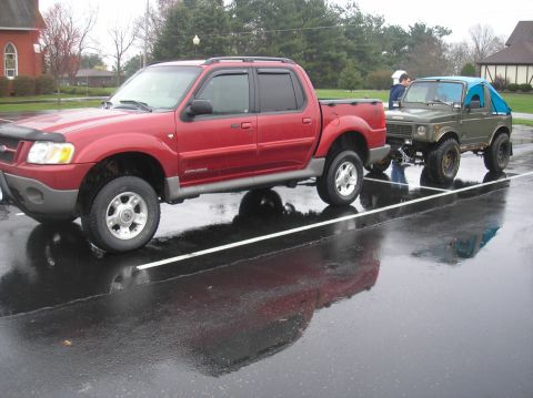 1987 Suzuki Samurai - A red Ford Explorer Sport Trac tows a green Suzuki Samurai on a wet day.