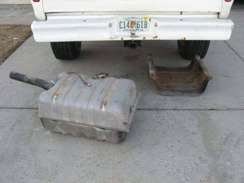 1979 Ford Bronco - Fuel tank and bracket removed from beneath a white vehicle.