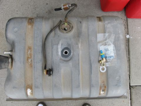 1979 Ford Bronco - A fuel tank is shown with a fuel filter and various fittings, resting on a concrete surface.