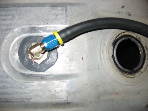 1979 Ford Bronco - Close-up of a fuel line fitting connected to a metal tank, likely part of a vehicle's fuel system.