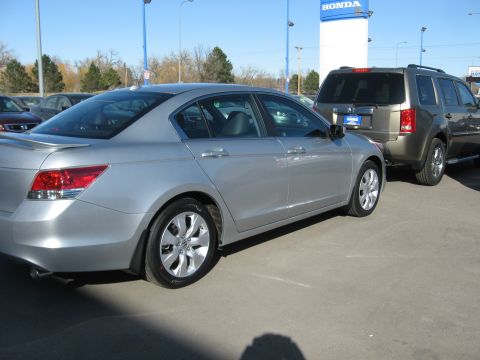 2009 Honda Accord - A silver sedan is parked next to a tan SUV in a lot with a Honda dealership sign in the background.