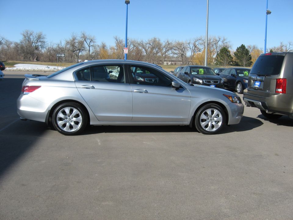 Silver sedan parked on asphalt lot, side view. Visible damage on front fender
