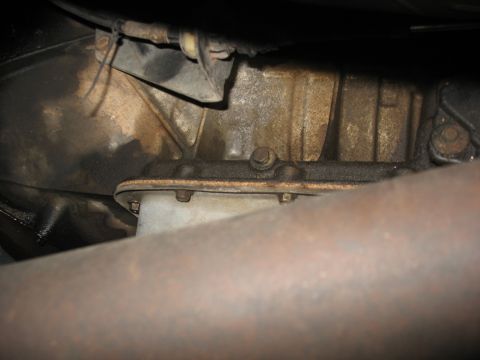 1995 Ford C-350 (Centurion Conversions) - Close-up view of a vehicle's transmission pan and casing, with visible oil stains and a section of exhaust pipe.