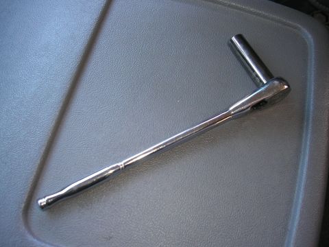 1995 Ford Bronco - A close-up view of a chrome ratchet and socket tool set on a textured gray surface.