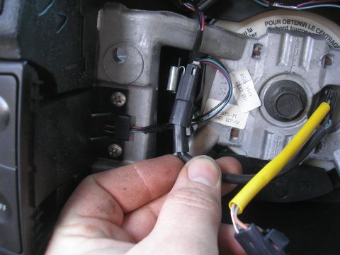 1995 Ford Bronco - Close-up of a hand disconnecting electrical connectors from a vehicle's steering wheel column.