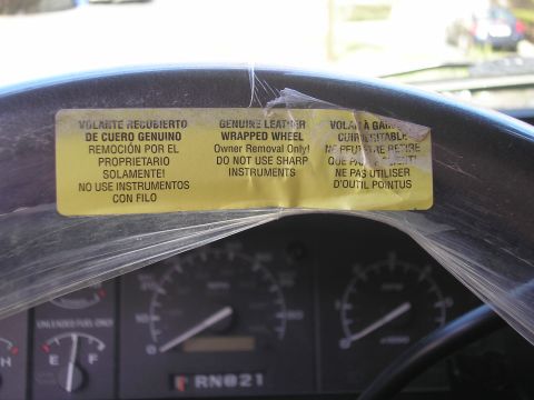 1995 Ford Bronco - A yellow sticker on a steering wheel provides instructions for its removal, indicating it's a genuine leather-wrapped wheel.