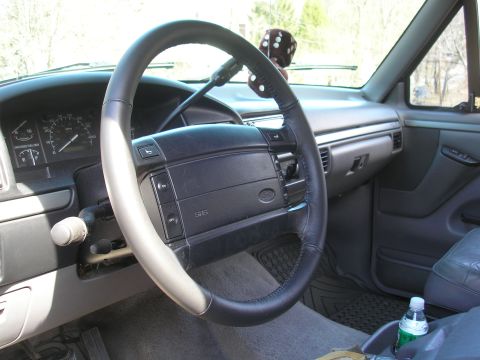 1995 Ford Bronco - The interior of a 1992 Ford F-Series truck, a leather-wrapped steering wheel and a dice air freshener hanging from the rearview mirror.
