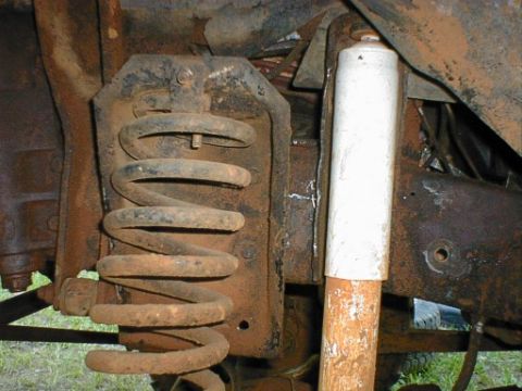 1979 Ford F-150 - Close-up view of a heavily rusted front suspension coil spring and a white shock absorber, likely from an older truck.