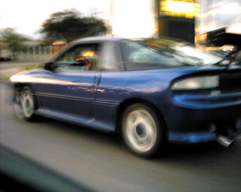 1990 Ford Taurus - A blue coupe with a spoiler is captured in motion, showing significant motion blur.