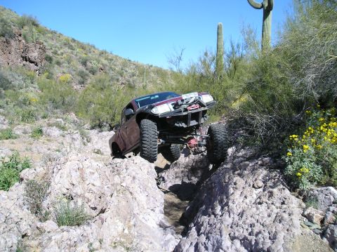 1986 Toyota Hilux - A modified pickup truck navigates a rocky desert trail with saguaro cacti in the background.