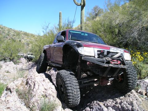 1986 Toyota Hilux - This heavily modified pickup truck is shown off-roading in a desert environment with other vehicles visible in the background.