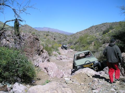 1986 Toyota Hilux - Two off-road vehicles traverse a desert path under a clear blue sky.