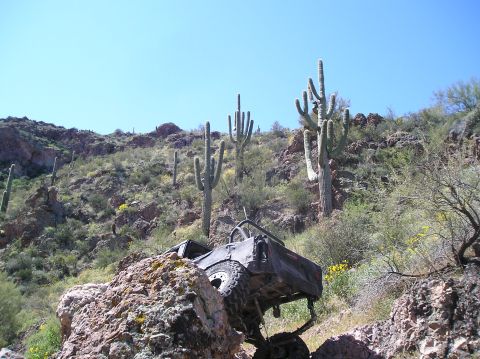 1986 Toyota Hilux - An off-road vehicle is stuck on a rocky incline in a desert environment, surrounded by saguaro cacti.