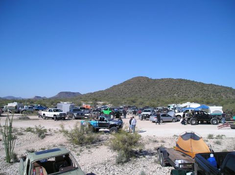 1986 Toyota Hilux - A gathering of off-road vehicles and camping equipment is set up in a desert environment with mountains in the background.