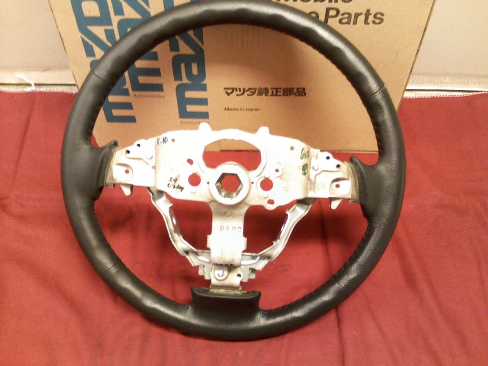 Steering wheel with black leather grip and metal hub, part number visible