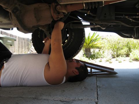 1986 Ford Bronco - A person works on the rear suspension components of a vehicle, which is elevated on ramps.