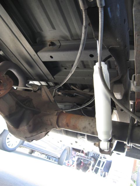 1986 Ford Bronco - The undercarriage of a vehicle, a rear differential and a white shock absorber, with another vehicle partially visible in the background.