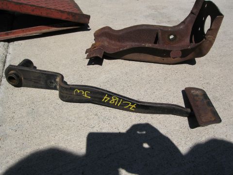 1986 Ford Bronco - Two rusty metal automotive parts, including a pedal assembly with yellow markings, lie on a concrete surface.
