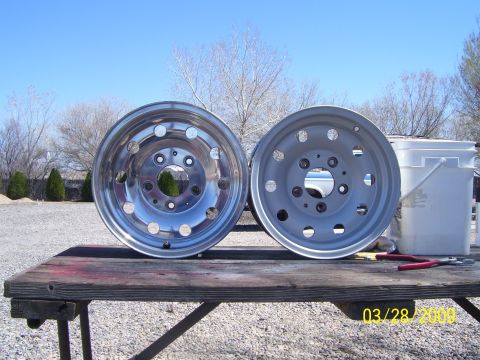 1993 Ford Bronco - Two wheels, one polished and one painted, sit on a weathered wooden table outdoors.