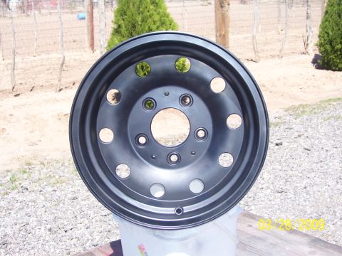 1993 Ford Bronco - A single black steel wheel is shown in an outdoor setting, resting on a white container.