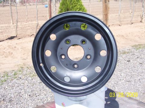 1993 Ford Bronco - A close-up view of a freshly painted black wheel, resting on a bucket outdoors.