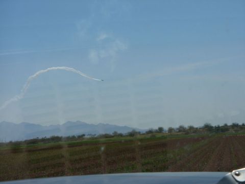 1978 Ford Bronco - An airplane performs aerobatics, leaving a smoke trail against a clear blue sky, with mountains in the background.