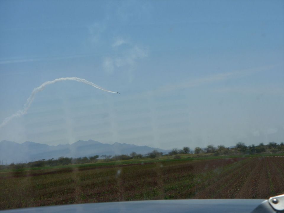 Airplane trailing smoke across a blue sky over fields and mountains