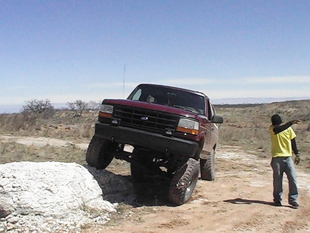 1992 Ford Bronco climbing over a rock on a dirt trail, person standing nearby pointing