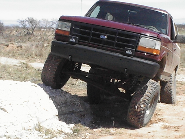 Maroon 1992 Ford Bronco climbing over a dirt mound off-road