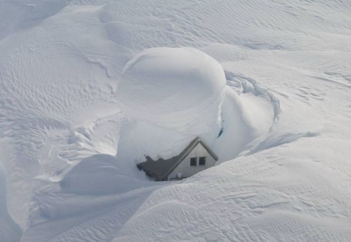 Small house almost completely covered by deep snow drifts