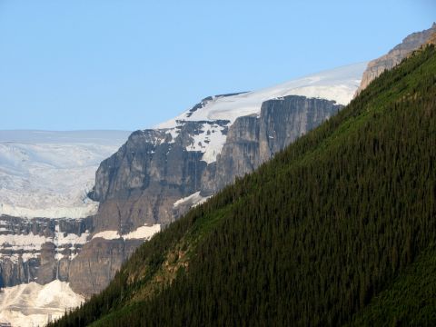 1995 Ford Bronco - A vast mountain landscape features a snow-capped peak and a glacier overlooking a steep, tree-covered slope under a clear blue sky.