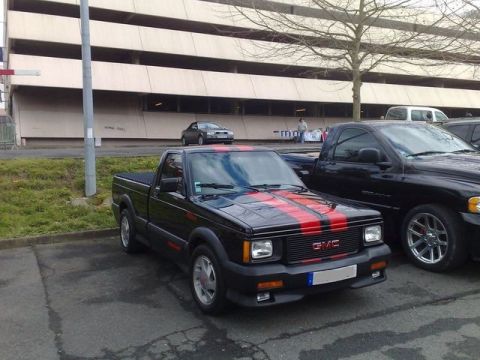 1991 Ford Crown Victoria - A black GMC Syclone pickup truck with red racing stripes is parked in front of a building.