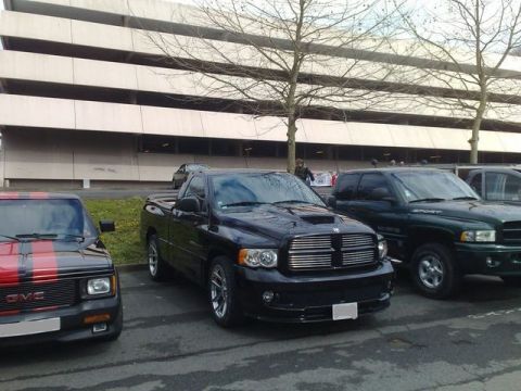 1991 Ford Crown Victoria - A black Dodge Ram pickup truck is parked in front of a building, with other vehicles to its left and right.