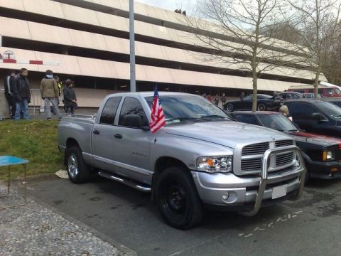 1991 Ford Crown Victoria - A silver Dodge Ram pickup truck is parked in front of a multi-story building, with other vehicles visible in the background.