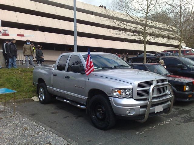 Silver Dodge Ram pickup truck parked in front of a building, with an American flag on the fender