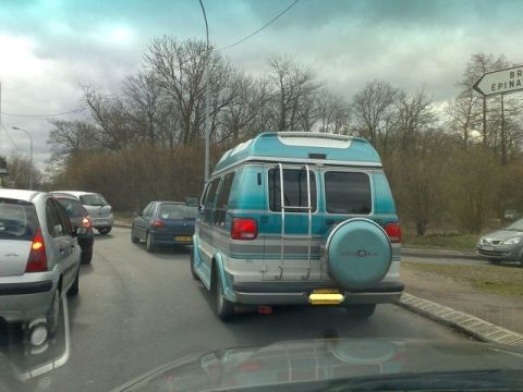 1991 Ford Crown Victoria - A blue and silver van is stuck in traffic behind other vehicles on a cloudy day.